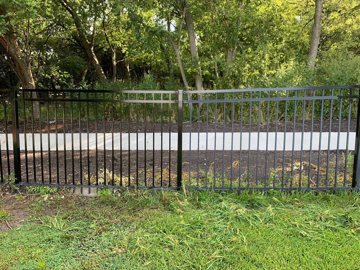 Wrought iron fence panel showing faded, worn finish on one side and freshly restored glossy black finish on the other