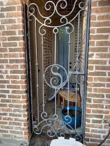 Ornate scrollwork iron gate with S monogram showing faded, weathered gray finish before restoration