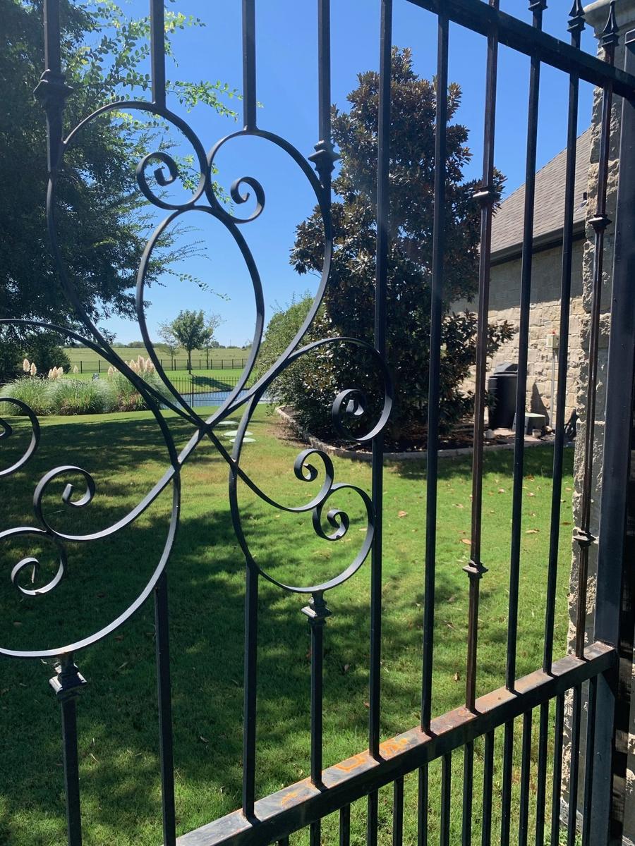 Close-up of ornate scrollwork iron gate with rust on the bottom rail before repair