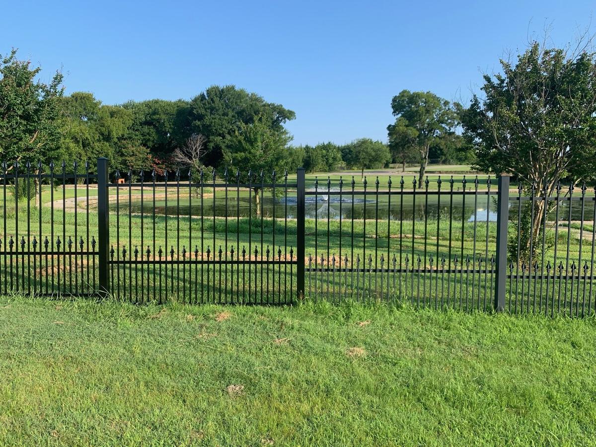 Restored black double-picket wrought iron fence with spear finials overlooking a pond with fountain