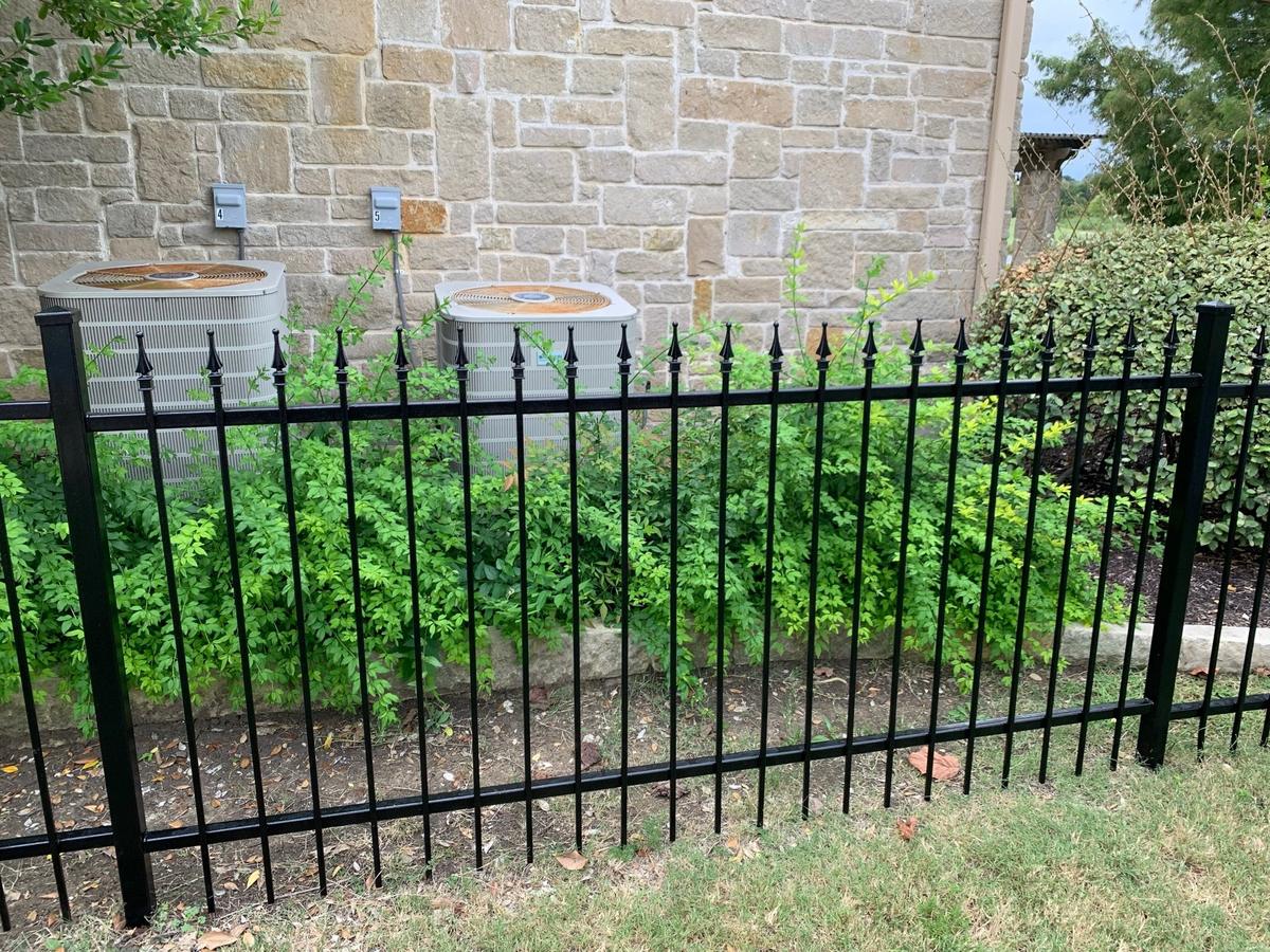 Glossy black spear-top wrought iron fence in front of a stone home landscape bed
